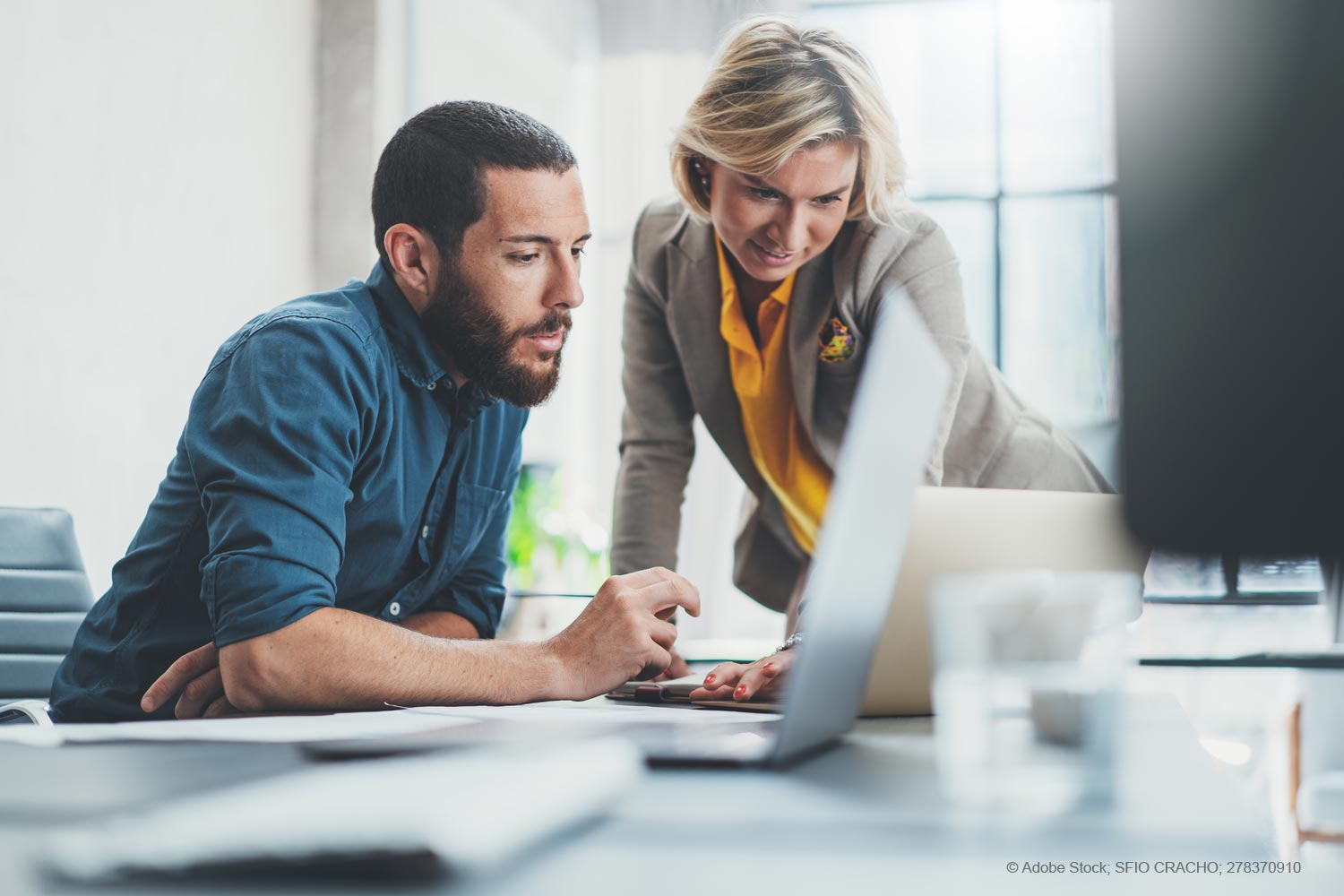 Eine Frau und ein Mann im Arbeitskontext, die gemeinsam an einem Projekt oder einer Idee arbeiten. Sie schauen gemeinsam auf einen Notebook-Bildschirm.